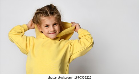 Portrait Of A Joyful Active Little Girl Wearing A Hood On A White Background. Happy Cute Child In A Yellow Sports Hoodie White Background. Sportswear Advertising Concept. Banner.