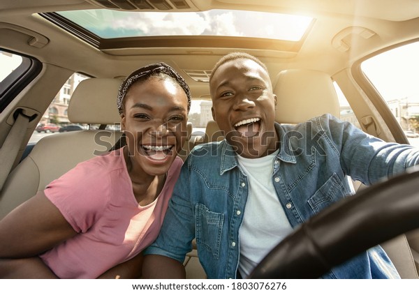 Portrait of joyful african couple in car, enjoying\
road trip, sun flare