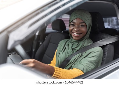 Portrait of joyful african muslim woman in car, enjoying road trip, smiling black islamic lady in hijab driving her new vehicle, holsing steering wheel and smiling at camera, closeup shot