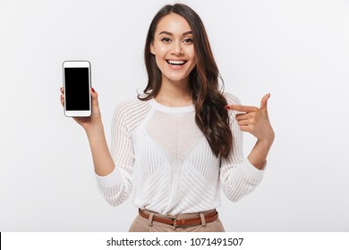 Portrait of a joyful asian businesswoman showing blank screen mobile phone isolated over white background