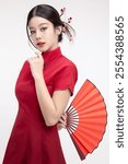 Portrait of joyful beauty Asian woman in red Cheongsam Chinese traditional dress holding red fan isolated on white background for Chinese New Year festival content.