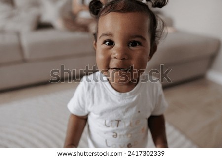 Portrait of joyful biracial toddler girl in room. Afro-Caucasian little girl. Concept of interracial family.