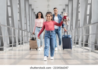 Portrait Of Joyful Cute Middle Eastern Girl Walking At Airport With Parents, Happy Young Arabic Family Ready For Vacation Trip Together, Going To Departure Gate At Terminal, Selective Focus On Kid
