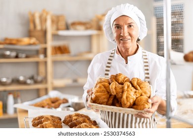 Portrait of joyful elderly woman holding wicker basket with bunch of freshly cooked croissants. - Powered by Shutterstock