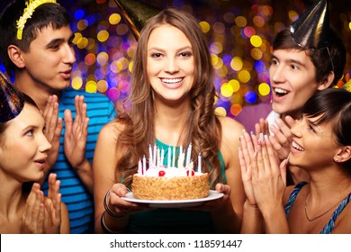 Portrait of joyful girl holding birthday cake surrounded by friends at party - Powered by Shutterstock