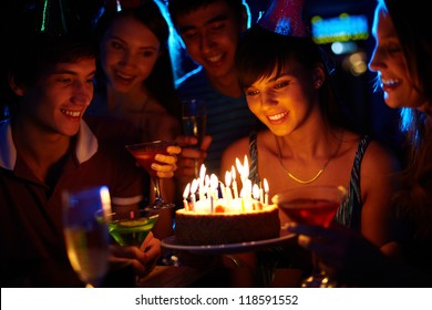 Portrait of joyful girl looking at birthday cake surrounded by friends at party