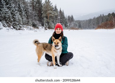 Portrait of a joyful girl and a red dog. The dog and the hostess walk through the snowy valley next to the forest. Winter walks in the fresh air