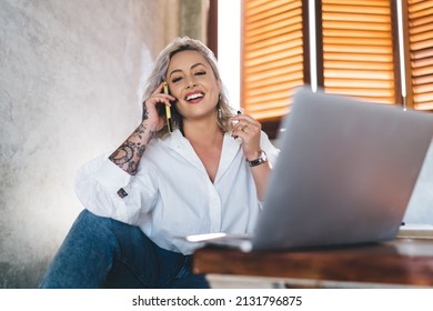 Portrait of joyful hipster girl smiling at camera during positive cell communication via smartphone application, cheerful female millennial with laptop computer posing while making friendly calling - Shutterstock ID 2131796875