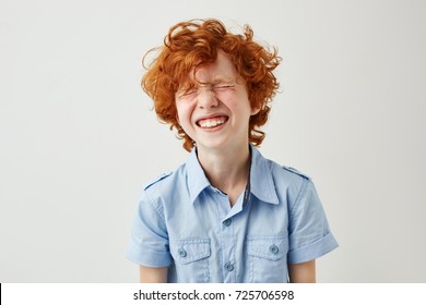 Portrait of joyful little boy with ginger hair and freckles laughing out loud with closed eyes in classroom during break.