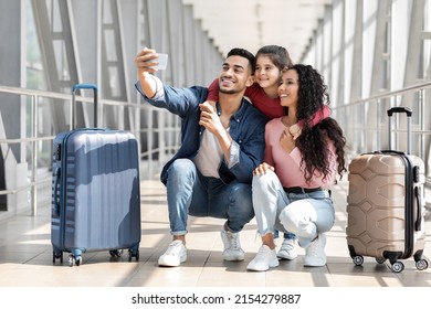 Portrait Of Joyful Middle Eastern Family Of Three Taking Selfie With Smartphone In Airport Terminal, Happy Arab Parents And Little Daughter Posing To Camera While Sitting Next To Suitcases - Shutterstock ID 2154279887