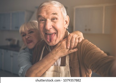 Portrait of joyful senior married couple having fun in cook room. They are taking photo of themselves and laughing while cuddling - Powered by Shutterstock