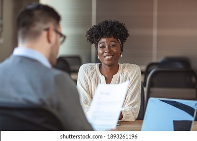 Portrait of joyful  woman smiling and holding resume while sitting in front of businessman during corporate meeting or job interview - business, career and placement concept