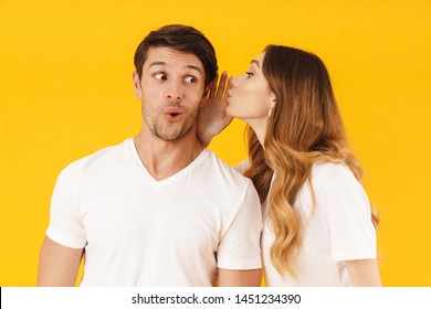 Portrait Of Joyful Woman Whispering Secret Or Interesting Gossip To Excited Man In His Ear Isolated Over Yellow Background