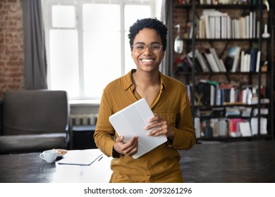 Portrait Of Joyful Young African American Woman In Eyeglasses Holding Digital Computer Tablet In Hands, Posing In Modern Loft Style Workplace, Feeling Motivated, Modern Tech Usage For Business.