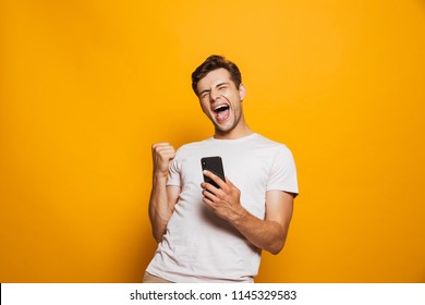 Portrait of a joyful young man holding mobile phone isolated over yellow background, celebrating - Powered by Shutterstock