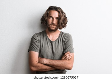 Portrait Of A Joyful Young Man With Long Wavy Hair In A Studio Arms Crossed.