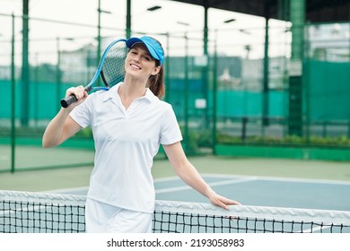 Portrait of joyful young woman posing with tennis racket at net on outdoor court - Powered by Shutterstock