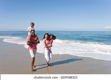 Portrait Of A Joyous Family Of Four Walking On Beach With Children In The Arms Of Parents With Copy Space.