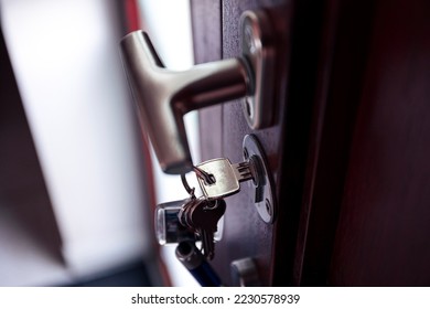 A portrait of a key in a key hole turned horizontally to lock or unlock a wooden front door with a T shaped door handle to keep other people, thieves or burglars out for safety and security. - Shutterstock ID 2230578939