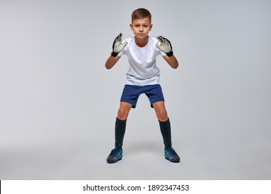 Portrait Of Kid Boy Goalkeeper Is Ready To Catch Soccer Ball, Stand In Pose, Isolated On Gray Background, Wearing Uniform