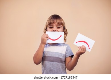 A Portrait Of Kid Boy Holding Cards With Mood Expression. Sad And Good Smile. Childhood And Emotion Concept