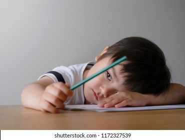 Portrait Kid Boy Holding Colour Pencil Sitting Alone And Looking Out With Bored Face,Preschool Child Laying Head Down On Table With Sad Face,Five Years Old Kid Bored With School Homework,spoiled Child