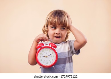 A Portrait Of Kid Boy Holding Red Alarm Clock. Childhood And Time Management Concept