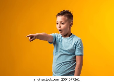 Portrait of kid boy mocking and teasing at someone showing finger at camera over yellow background. Bulling concept