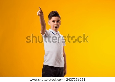 Portrait of kid boy mocking and teasing at someone showing finger at camera over yellow background. Bulling concept