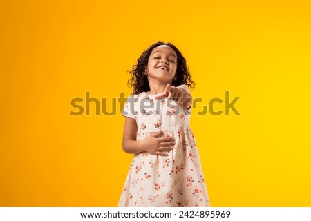 Portrait of kid girl mocking and teasing at someone showing finger at camera and holding stomach over yellow background. Bulling concept