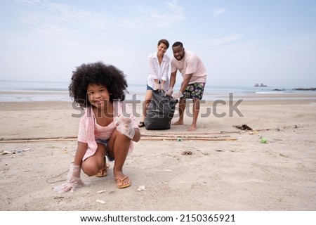 Portrait of kid girl picking up garbage waste on the beach with father and mother in background 