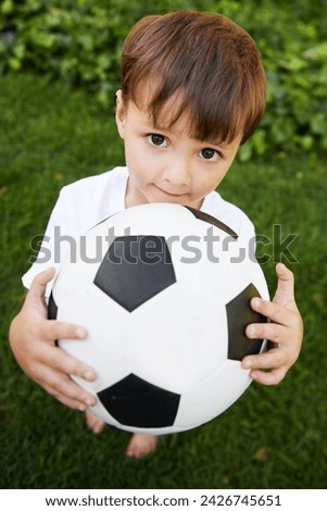 Portrait, kid and play with football in garden for fun, healthy and childhood development in Brazil. Closeup, sweet and young boy with soccer ball for afternoon game or exercise in backyard or park
