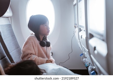 Portrait Of Kid Sitting On An Airplane And Watching Movie From The Screen At The Front Seat