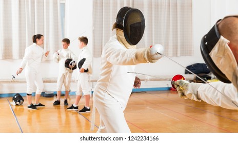 Portrait of kids and adults fencers with trainer engaged in fencing in training room