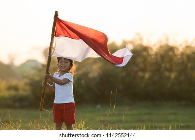 Portrait Of Kids Raising Indonesian Flag In Sunset Sky