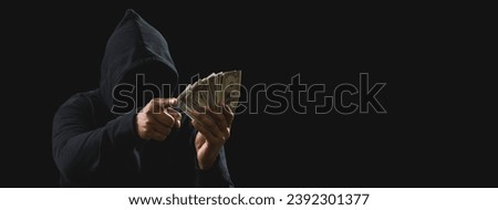 Portrait killer hacker mafia gangster spy man oneperson in black hoodie standing look hand holding money dollar obtained from robbery threat crime attack victim people night dark background copy space
