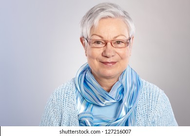 Portrait Of Kind Elderly Lady In Light Blue, Smiling, Looking At Camera.