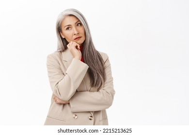 Portrait of korean businesswoman, woman with grey hair thinking, wearing suit, smiling intrigued, standing over white background - Powered by Shutterstock