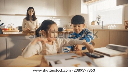Portrait of a Korean Children Sitting at a Kitchen Table, Drawing, Writing While Mother is Preparing Breakfast. Perfect Parenting of Little Cute Kids Waiting for Nutritious Meal Before Going to School