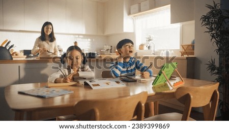 Portrait of a Korean Children Sitting at a Kitchen Table, Drawing and Writing While their Mother is Preparing Breakfast. Little Cute Kids Waiting for Nutritious Meal Before Going to School