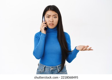 Portrait Of Korean Woman With Confused Face Talking On Mobile Phone, Having A Call, Talking With Puzzled Face On Telephone, White Background