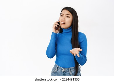 Portrait Of Korean Woman With Confused Face Talking On Mobile Phone, Having A Call, Talking With Puzzled Face On Telephone, White Background.