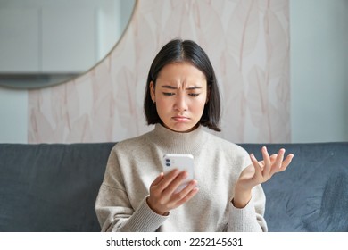Portrait of korean woman looking at smartphone with puzzled face, cant understand smth strange on mobile phone. - Shutterstock ID 2252145631