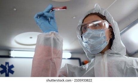 Portrait Of Lab Technician Holding Tube Of Blood Sample In Mobile Laboratory. Female Scientist Providing Blood Test For Coronavirus. Paramedic Doctor Wearing Protective Suit, Glasses And Mask At Work