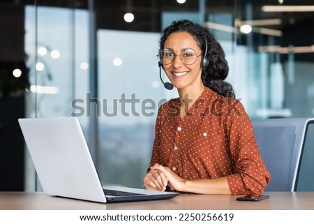 Portrait of Latin American business woman, office worker looking at camera and smiling, using headset and laptop for remote online communication, customer support tech call center worker.
