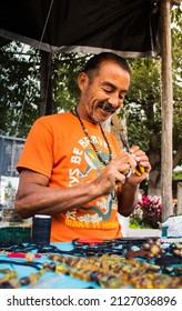 Portrait latin artisan man making a handmade brasalete at a street stall near a park 