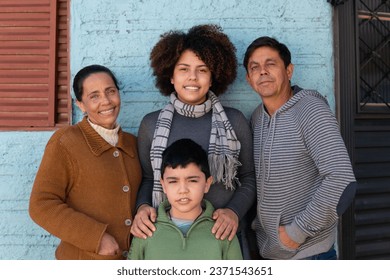 Portrait of latin multigenerational family standing and looking at camera outside the house. Affectionate, bonding, love, generation concept.