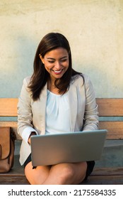 Portrait Of A Latina Teacher Sitting On A Bench And Working Happily With Her Computer In The Street. Copy Space