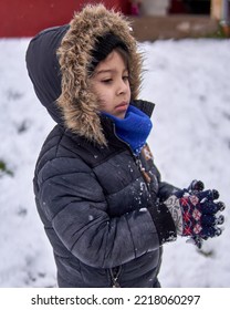 Portrait Of Latino Little Boy In Profile With Worried Face And Clasping His Gloved Hands Together, In Winter In The Snow, Wearing A Furry Hooded Coat And Blue Scarf