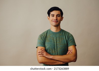 Portrait latino man with arms crossed and black hair smiling handsome young adult green t-shirt over gray background looking at camera studio shot - Powered by Shutterstock